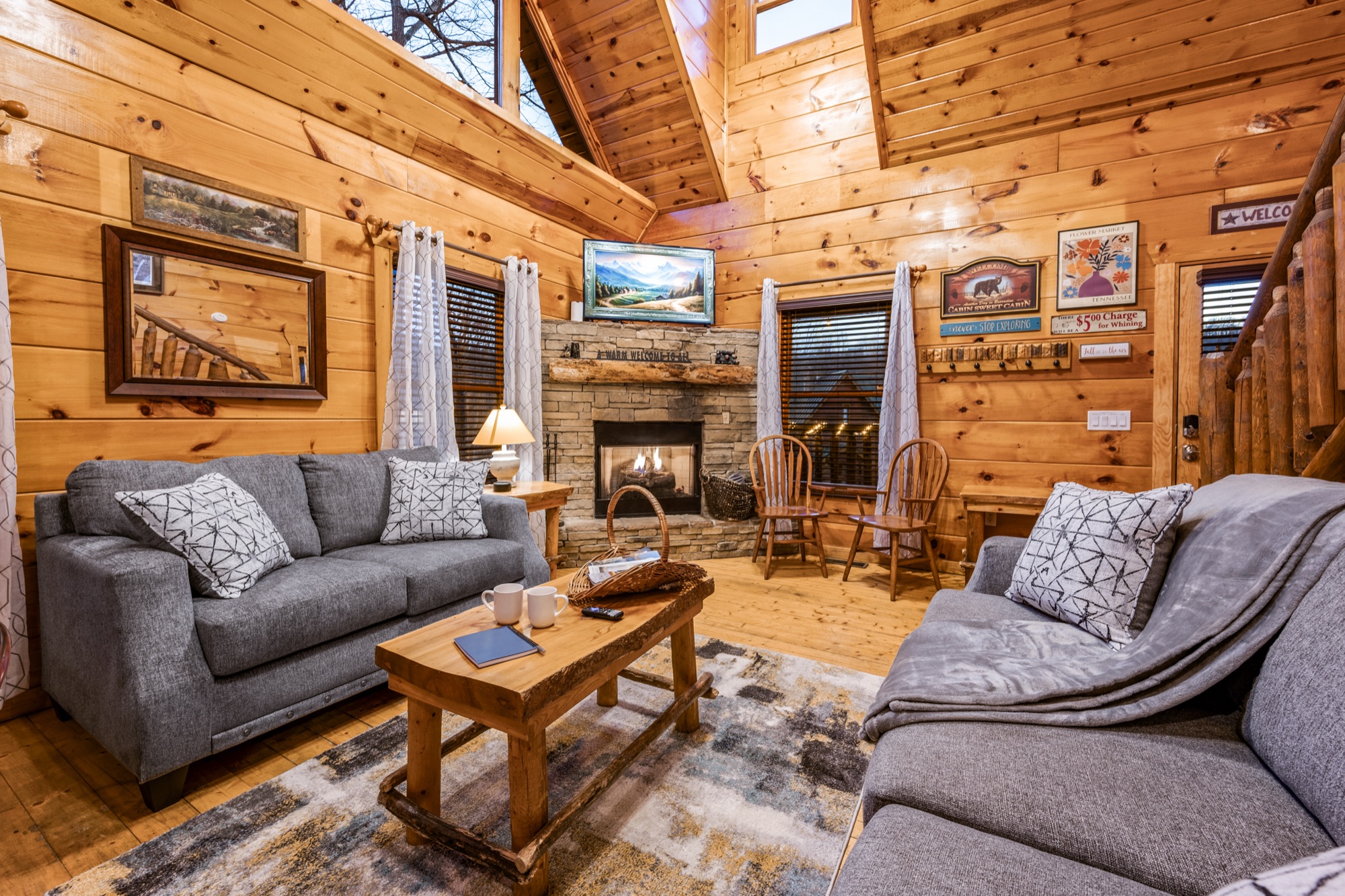 Bearadise living room with two gray sofas facing a stone fireplace under a wood plank vaulted ceiling